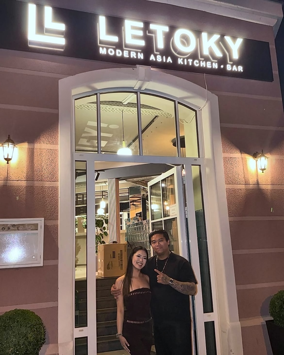 Die Geschwister, die LETOKY führen, am Abend vor dem beleuchteten Eingang des Restaurants